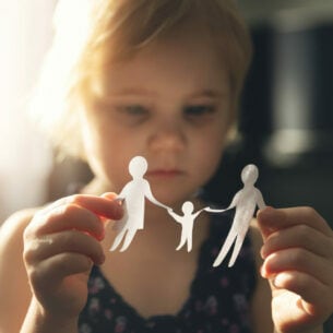Ein Mädchen hält ein Papierschnittmuster in der Hand, in dem ein Mann, eine Frau und ein Kind zu erkennen sind.
