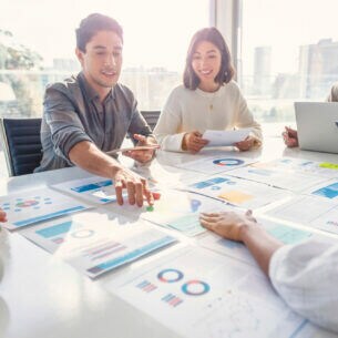 Mehrere Personen sitzen um einen Tisch und blicken auf mehrere Dokumente mit Statistiken und Analysen..