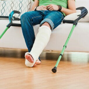 Aufnahme der Beine einer Person, die auf einem Sofa sitzt und ein eingegipstes Bein hat.