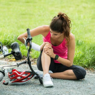 Eine Person hält sich ihr Knie, nachdem sie mit dem Fahrrad gestürzt ist.