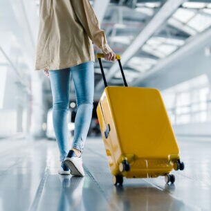 Eine Person in der Rückansicht zieht im Flughafen einen Koffer hinter sich her.