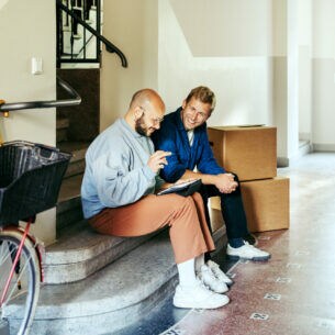Zwei Personen sitzen am Ende einer Treppe auf den Stufen und schauen auf ein Tablet.