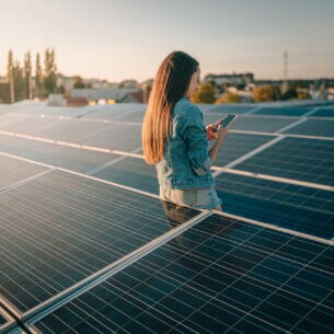 Eine Person steht zwischen mehreren Solarpanel und tippt auf ihrem Smartphone.