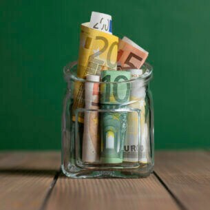 Nahaufnahme eines Glases, in dem mehrere Euroscheine stecken.