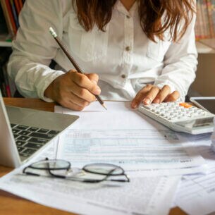 Eine Person sitzt am Schreibtisch und trägt mit einem Bleistift etwas in ein Dokument ein.
