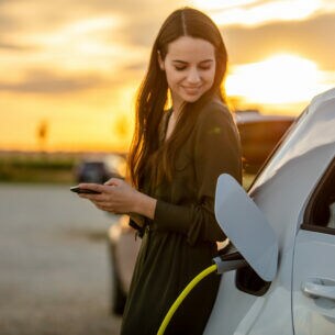 Eine Person lehnt an einem weißen E-Auto bei Sonnenuntergang.
