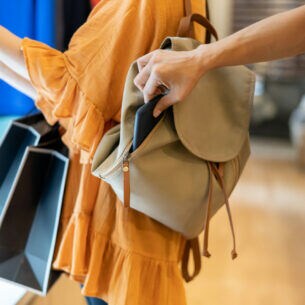 Nahaufnahme einer Hand, die ein Smartphone aus einem Rucksack entwendet.