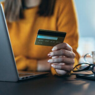 Nahaufnahme einer Person, die vor einem Laptop sitzt und eine Kreditkarte in der Hand hält.