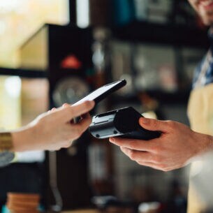 Eine Person bezahlt mit dem Smartphone kontaktlos an einem Terminal.