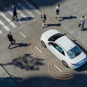 Ein Auto in der Aufsicht, das sich einem Zebrastreifen nähert, über den Personen laufen.