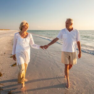 Zwei Personen gehen Hand in Hand am Strand entlang.