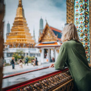 Eine Person blickt aus einem prunkvoll verzierten Fensterrahmen auf goldbesetzte Tempel.