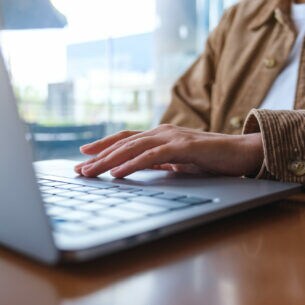 Eine Person sitzt am Tisch und bedient ein Notebook.