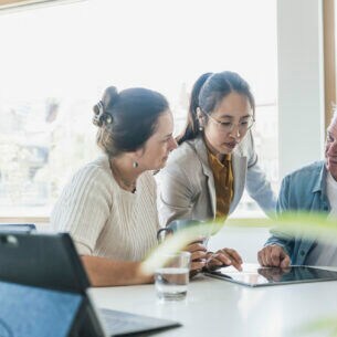 Drei Personen sind im Gespräch und haben ein Tablet auf dem Tisch vor ihnen liegen.