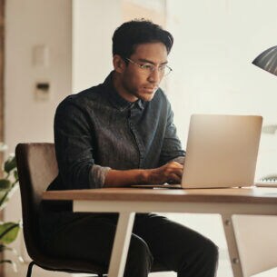 Eine Person sitzt vor einem geöffneten Laptop am Tisch.