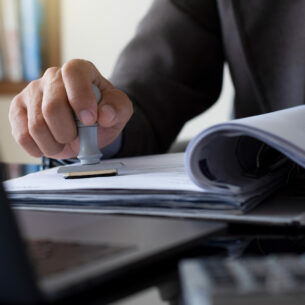 Eine Person in Anzug stempelt Dokumente in einem Ordner ab.