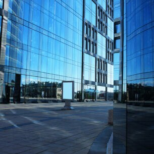 Mehrere verglaste Fassaden von modernen Bürogebäuden in der Sonne.