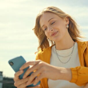 Eine junge Person sitzt im Freien und hält ein Smartphone in ihren Händen.