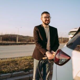 Eine Person steht vor ihrem Auto und hält den Zapfhahn fest, der im Auto steckt.