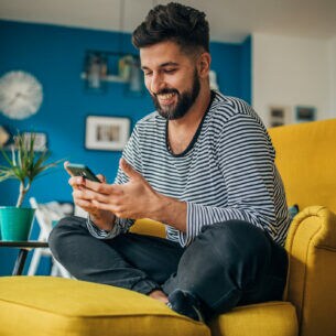 Eine Person sitzt im Schneidersitzt auf einem Sessel und blick auf das Smartphone in ihren Händen.