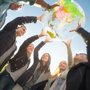 Eine Gruppe junger Leute halten gemeinsam ein Modell eines Globus in die Höhe.