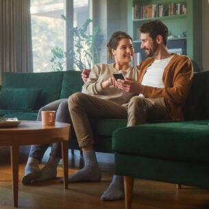 Zwei Personen sitzen nebeneinander auf einem Sofa und blicken gemeinsam auf ein Smartphone.