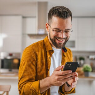 Eine Person hält ein Smartphone in den Händen und blickt lächelnd drauf.