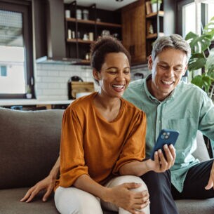 Zwei Personen sitzen gemeinsam auf einem Sofa und blicken zusammen auf ein Handy.