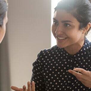 Zwei Mitarbeiterinnen mit verschiedenen kulturellen Hintergründen sitzen an einem Schreibtisch und führen ein Gespräch.
