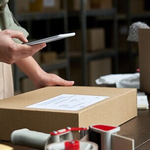 Frau im Paketlager breitet ein Paket für den Versand vor.