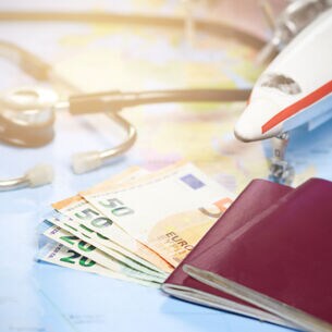 Artikelbild Weltkarte mit Geldscheinen, Reisepass, kleinem Flugzeug und Stethoskop