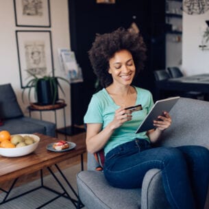 Person sitzt auf einem Sessel und schaut auf ihr Tablet und auf ihre Kreditkarte