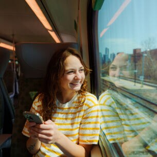 Person sitzt in der Bahn am Handy und schaut aus dem Zugfenster