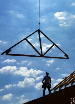 Ein Handwerker auf dem Dach und ein heranbefördertes Giebelteil aus Holz