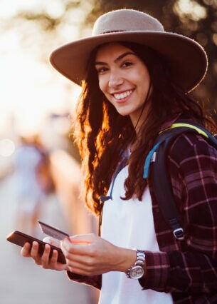 Eine lachende junge Frau mit Smartphone und Kreditkarte in der Hand