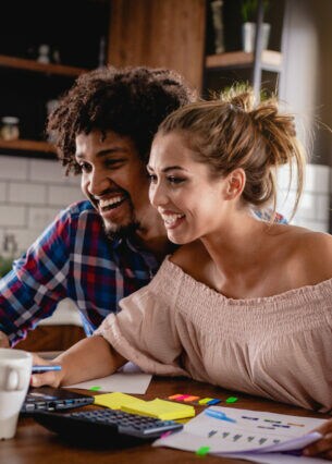 Ein junges Paar an einem Tisch vor einem Laptop mit Dokumenten vor sich ausgebreitet