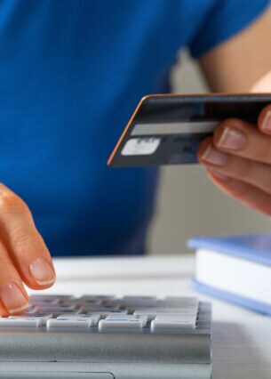 Eine Person hält eine Kreditkarte in der Hand und tippt mit der anderen Hand Daten auf einer Tastatur ein