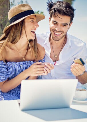 Ein fröhliches Pärchen sitzt im Urlaub am Laptop