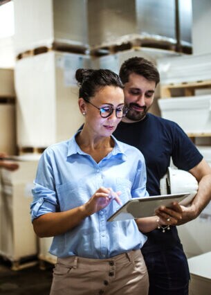 Frau mit Tablet in der Hand in einem Lager und ein Mann, der ihr über die Schulter aufs Tablet schaut