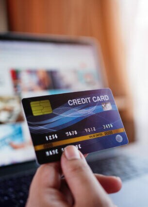 Zwei Hände, eine Kreditkarte und ein Flugzeugmodell haltend, vor einem Laptopbildschirm