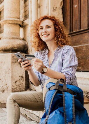 Junge Frau auf einer Treppe sitzend mit Kreditkarte und Smartphone in der Hand