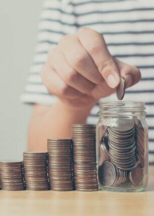 Von links nach rechts höher werdende Münzstapel und ein mit Geld gefülltes Glas