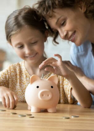 Eine Mutter und ihr Kind werfen Münzen in ein Sparschwein.