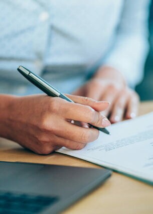 Person im hellen Businesshemd sitzt am Schreibtisch und unterschreibt ein Dokument