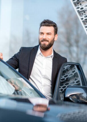 Lächelnder Mann im Anzug an der geöffneten Fahrzeugtür