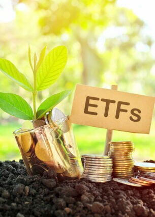 Auf Erde gestapelte Münzen, Schild mit Aufschrift ETFs und Münzen in einem Glas mit wachsender Pflanze im Vordergrund und grüner Natur im Hintergrund.