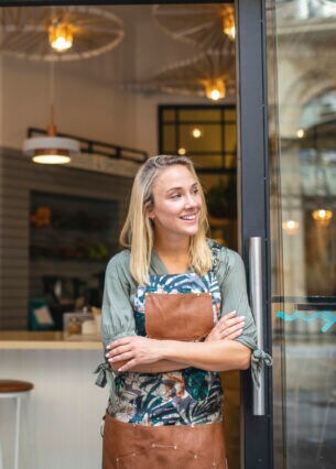 Eine Person mit Schürze lehnt im Eingangsbereich eines Geschäfts.