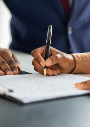Zwei Personen sitzen am Tisch, eine davon unterschreibt ein Dokument