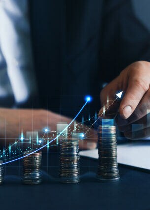 Businessmensch stapelt Münzen aufeinander, darübergelegt ein steigender Chart