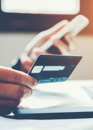 Ausschnitt einer Person, die am Laptop sitzt und eine Bankkarte in der Hand hält